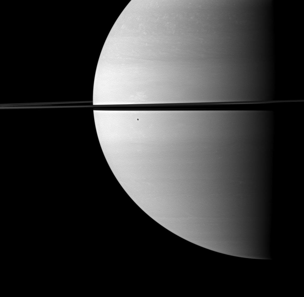 The shadow of Enceladus darkens a small portion of the swirling clouds on Saturn