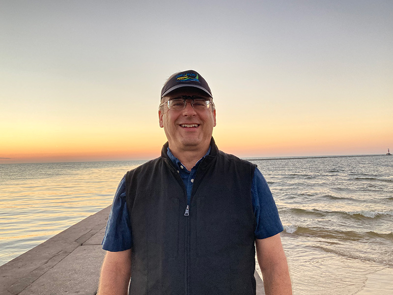 Craig Kundrot standing on a sidewalk with Lake Michigan behind him.