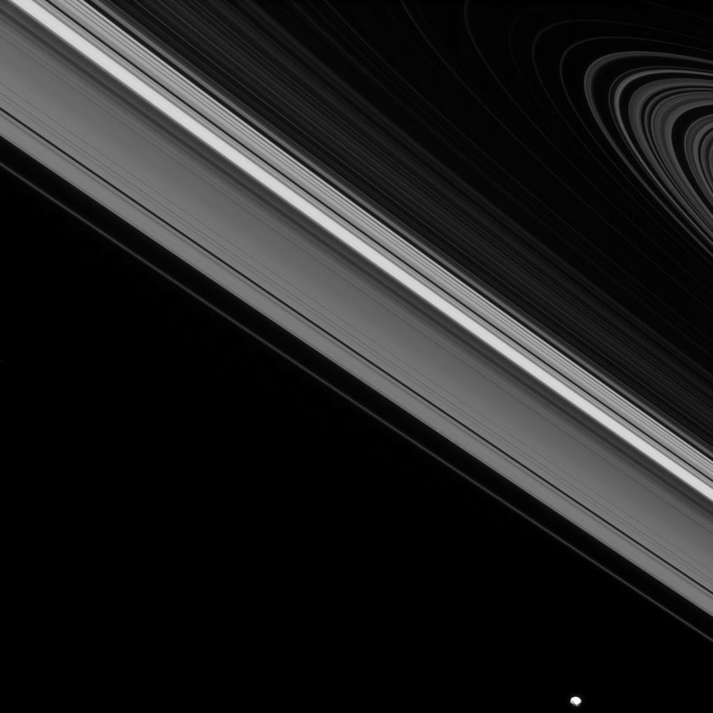 While the moon Epimetheus passes by, beyond the edge of Saturn's main rings, the tiny moon Daphnis carries on its orbit within the Keeler gap of the A ring.