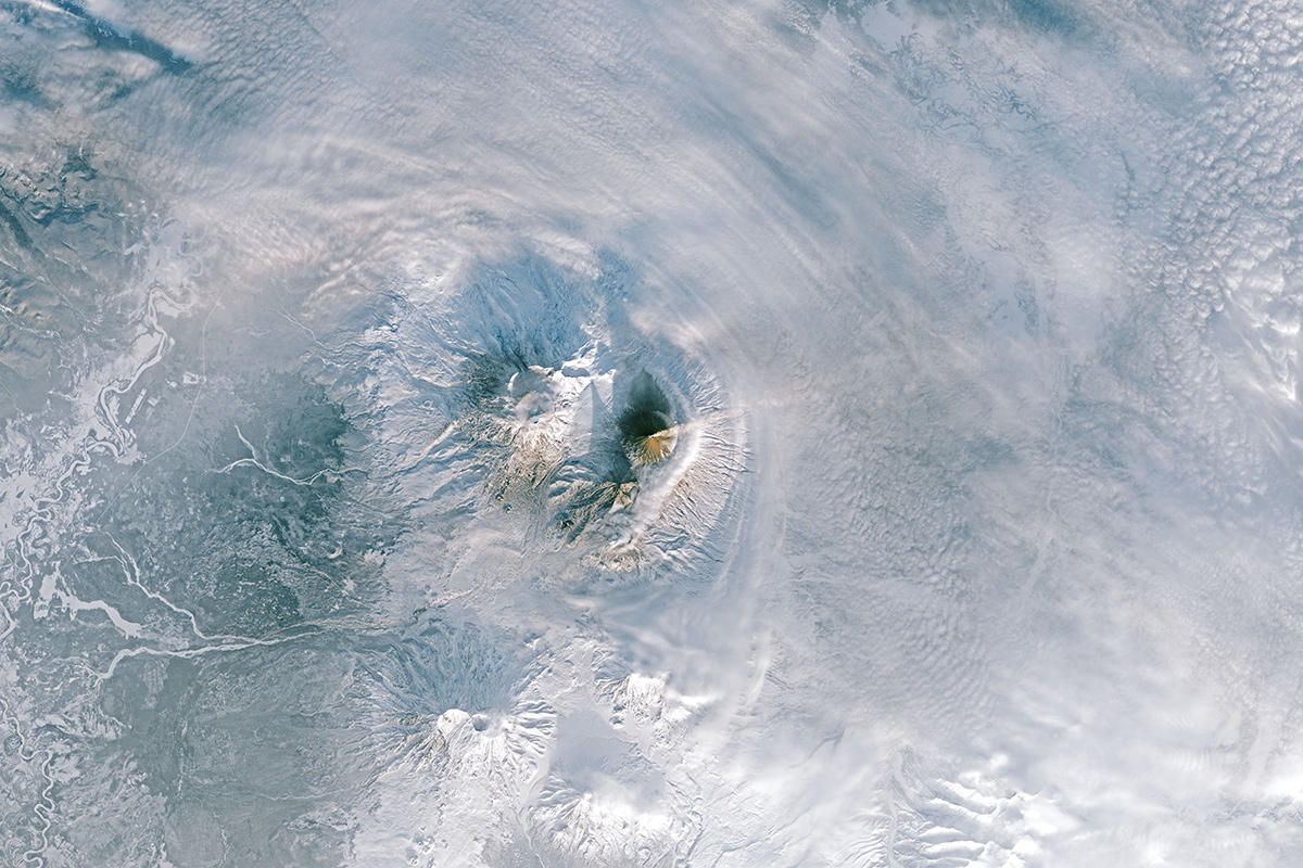 Aerial view of plumes rising over a volcano on a snow-covered landscape
