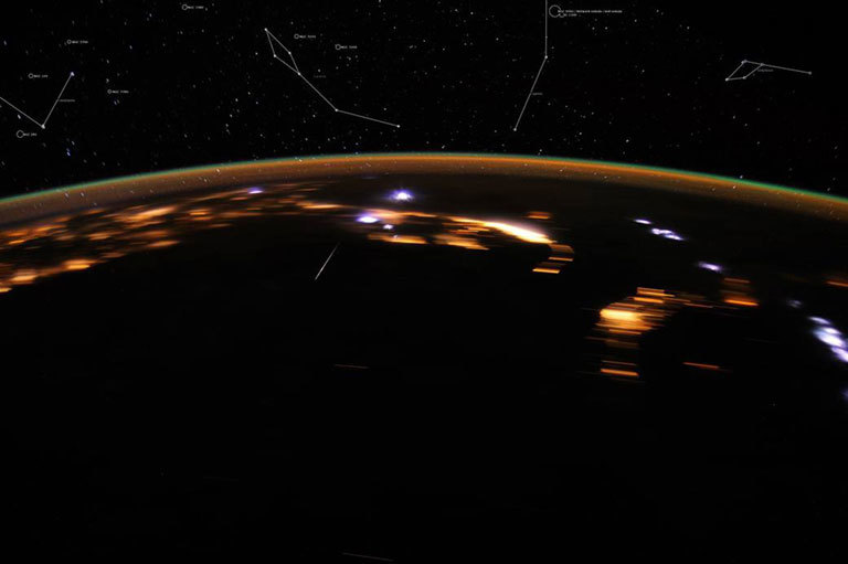 Bright white lights over Earth as meteors collide with the atmosphere. Stars can be seen in the night sky above the curvature of the planet. 
