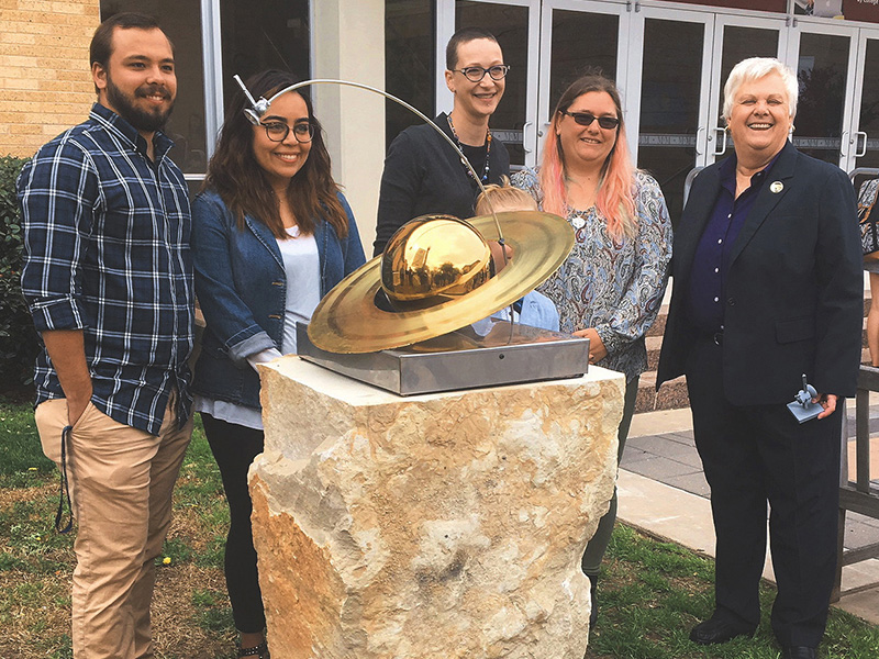 slide 1 - Group of smiling people surrounding a statue of Cassin and Saturn.