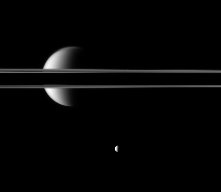Saturn's rings, partially darkened by the planet's shadow, cut a striking figure before Saturn's largest moon, Titan.