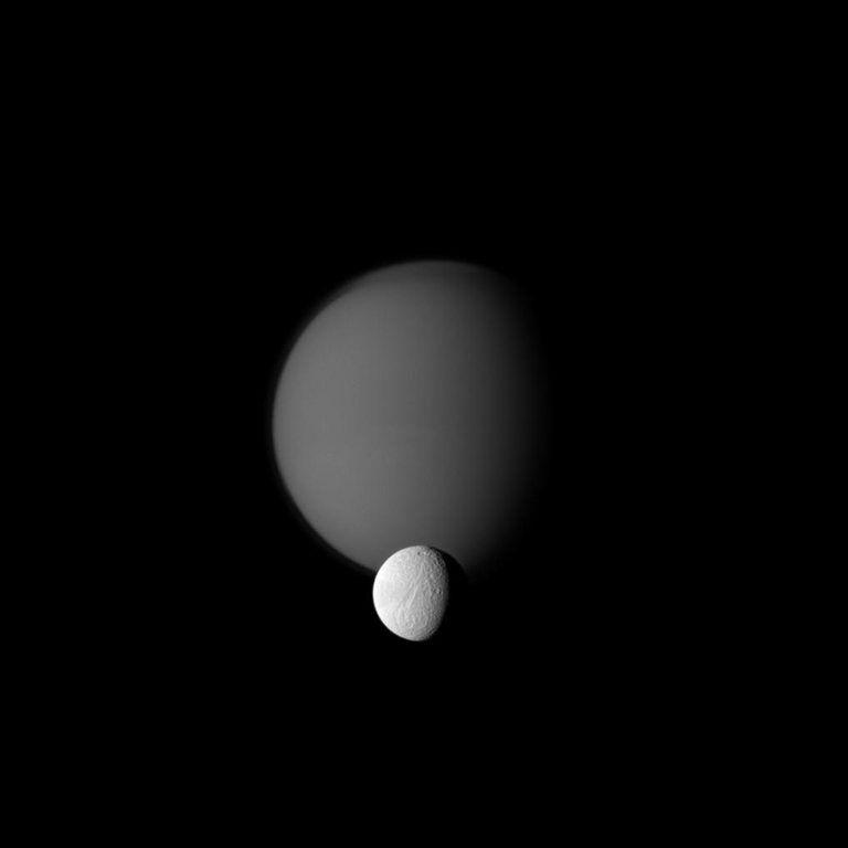 The Cassini spacecraft watches a pair of Saturn's moons, showing the hazy orb of giant Titan beyond smaller Tethys. The image was taken in visible green light with the Cassini spacecraft narrow-angle camera on Oct. 18, 2010.