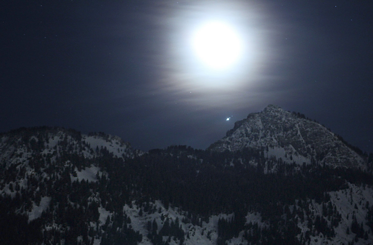 The Moon, lost in haze, rises over the Wasatch Mountains near Salt Lake City in February 2019. The planet Jupiter can be seen nearby, along with three of its moons. Credit: NASA/Bill Dunford  | › Full image and caption