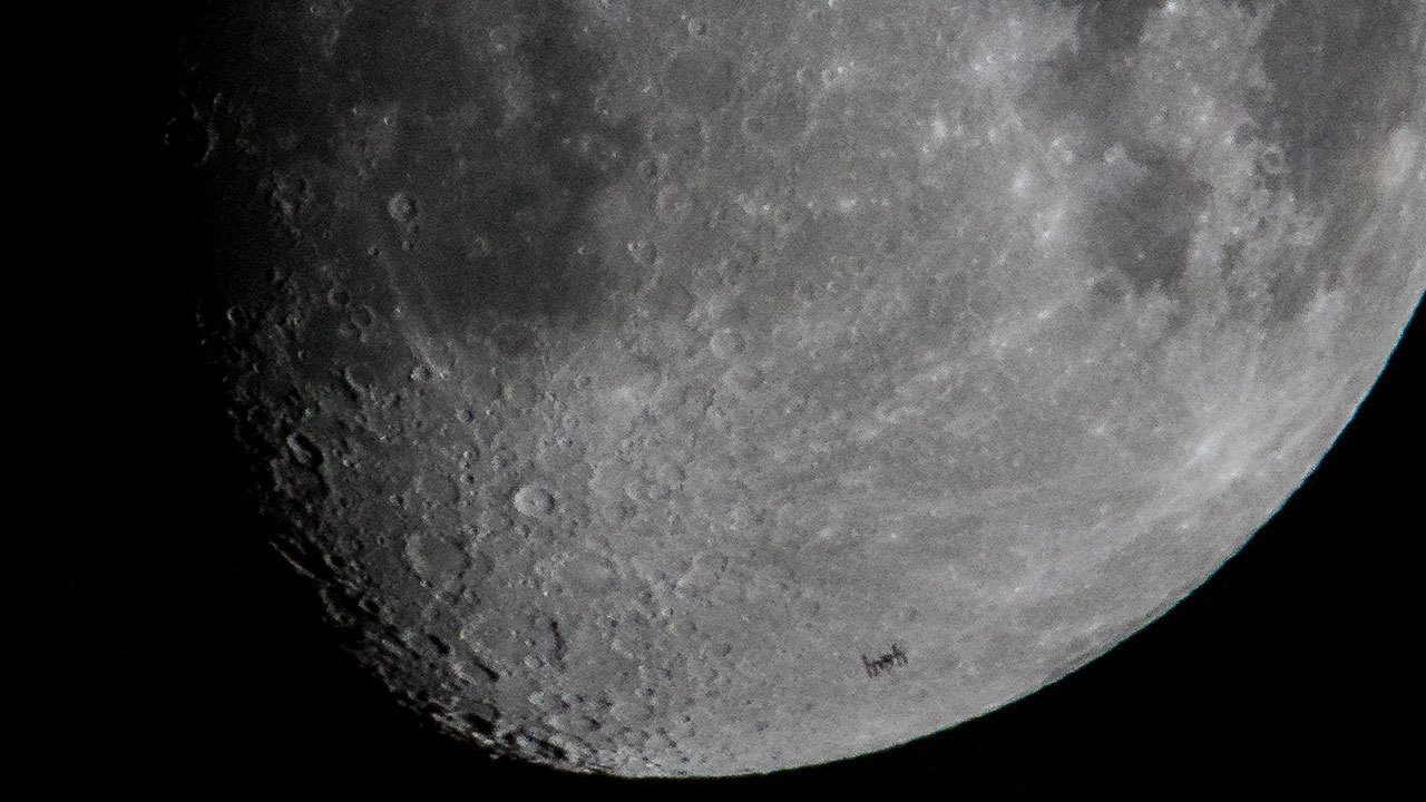 Close of image of moon with a small silhouette of the space station on the lower third.