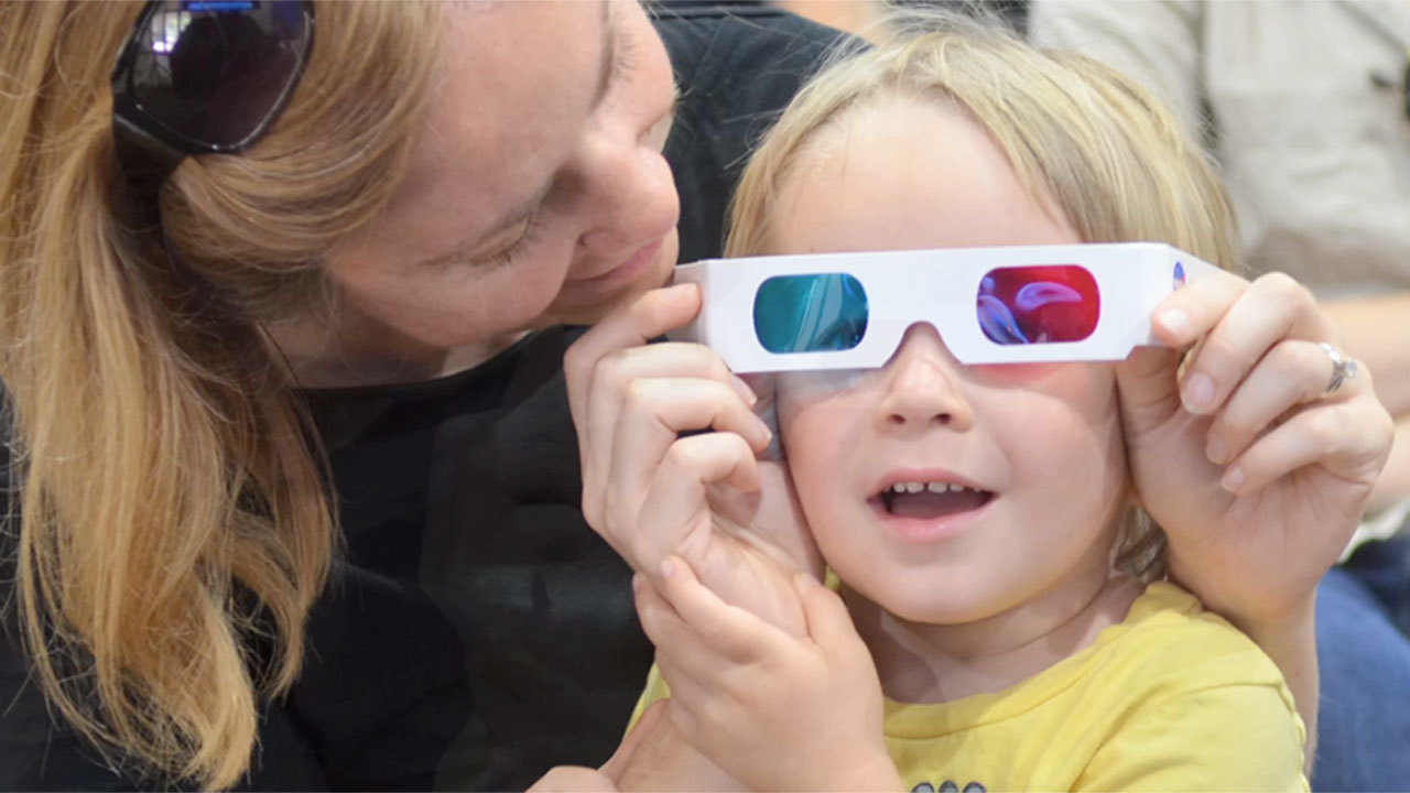 Woman holding 3D glasses on a young girl.