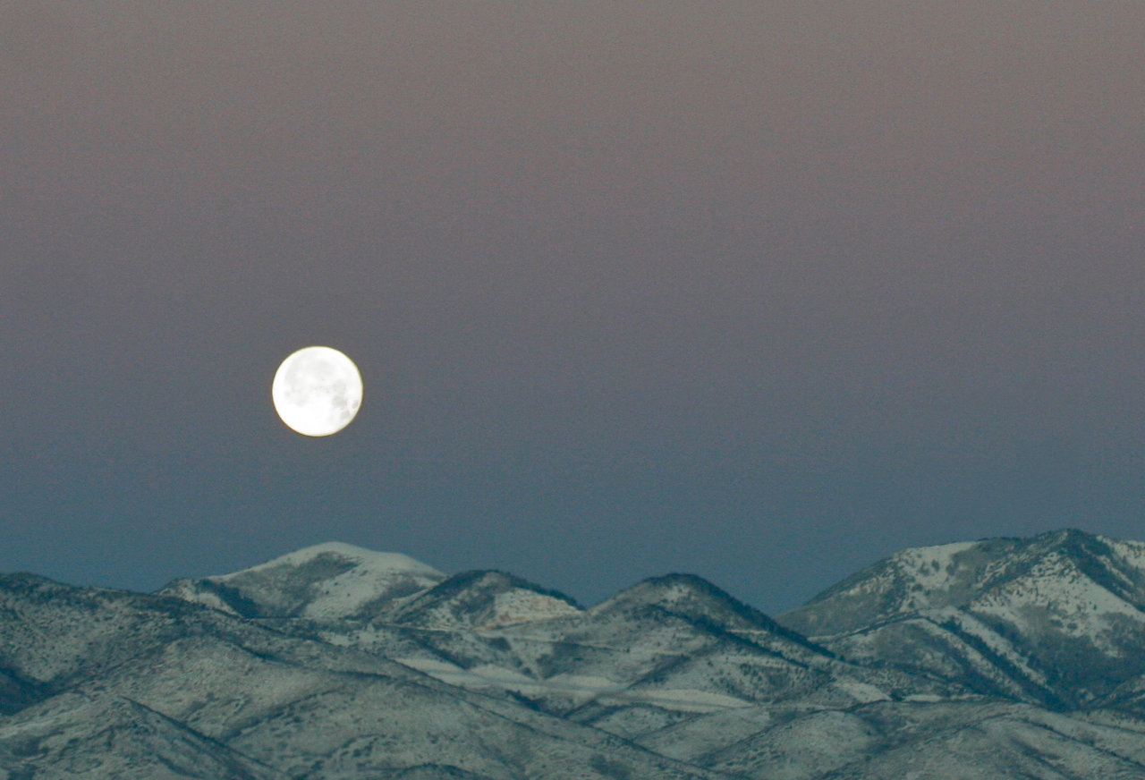 full moon setting over mountains