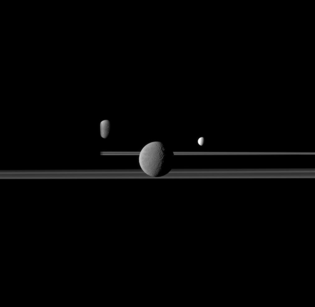 Cassini observes three of Saturn's moons set against the darkened night side of the planet. From left, Dione, partly obscured by Saturn, then Rhea and Enceladus. This view looks toward the northern, sunlit side of the rings from just above the ringplane.