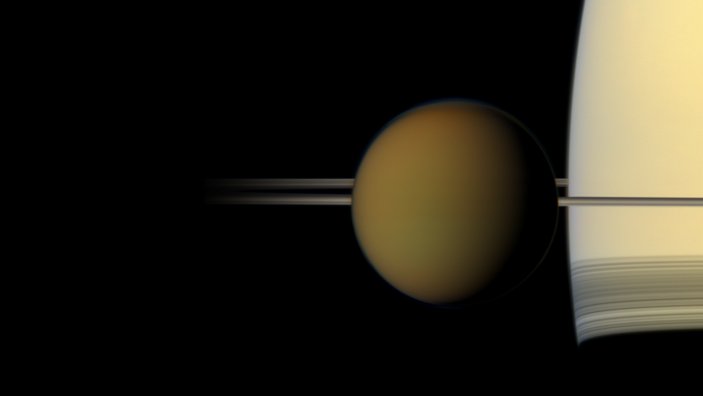 A color image of the hazy globe of Titan as it hangs in front of Saturn and its rings