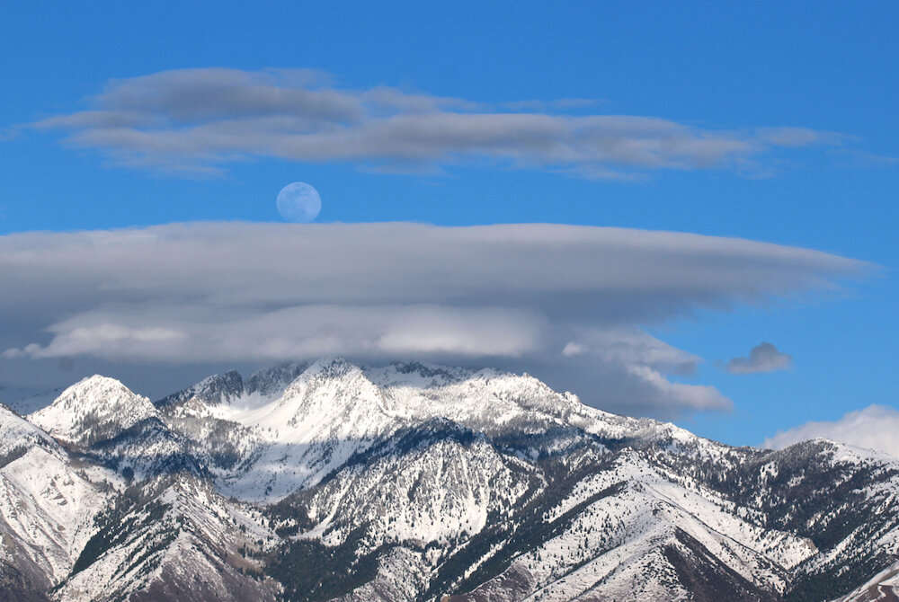 nearly full Moon rising over cloudy mountaintops 