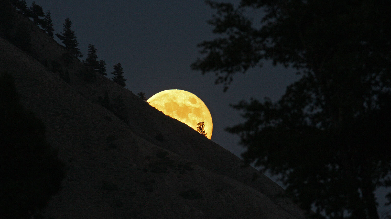 Full moon rising behind a steep slope.