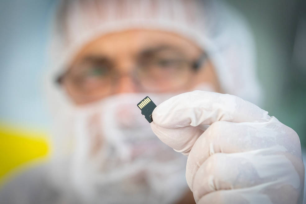 man in clean room suit holding a small chip