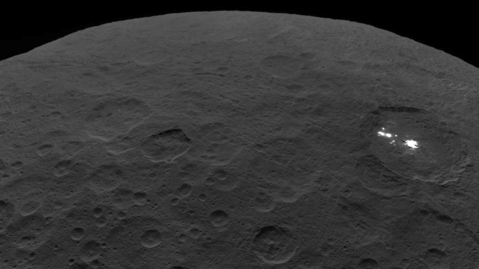 Close view of Ceres with bright white spot visible in crater.