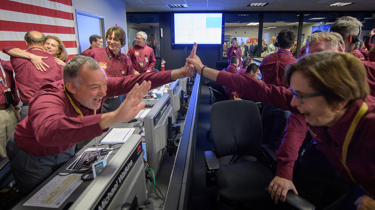 People cheering, high-fiving and hugging in mission control.