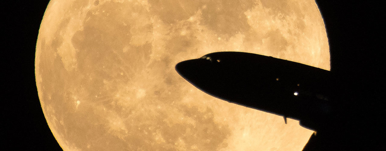 Airliner silhouetted in front of a full moon.