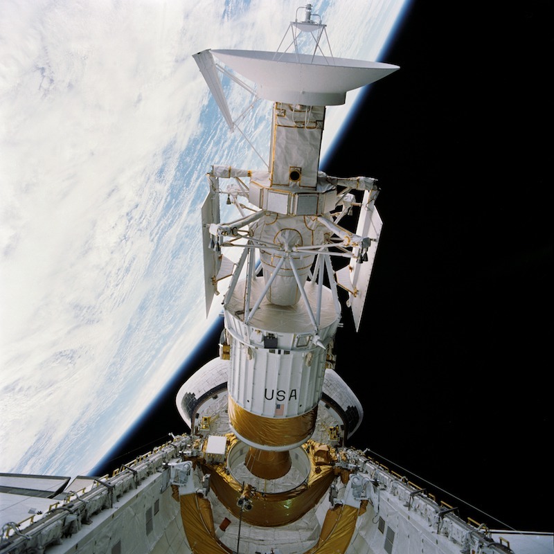 spacecraft leaving cargo bay of space shuttle with curving earth horizon in the background
