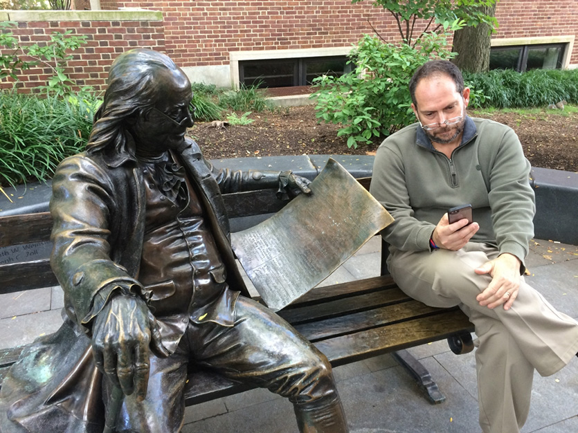 Man sitting on bench next to statue of Benjamin Franklin