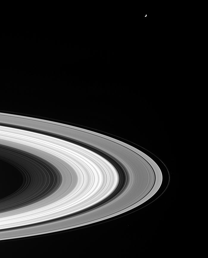 Black and white image of Saturn's rings with small white dot of Tethys hovering above.