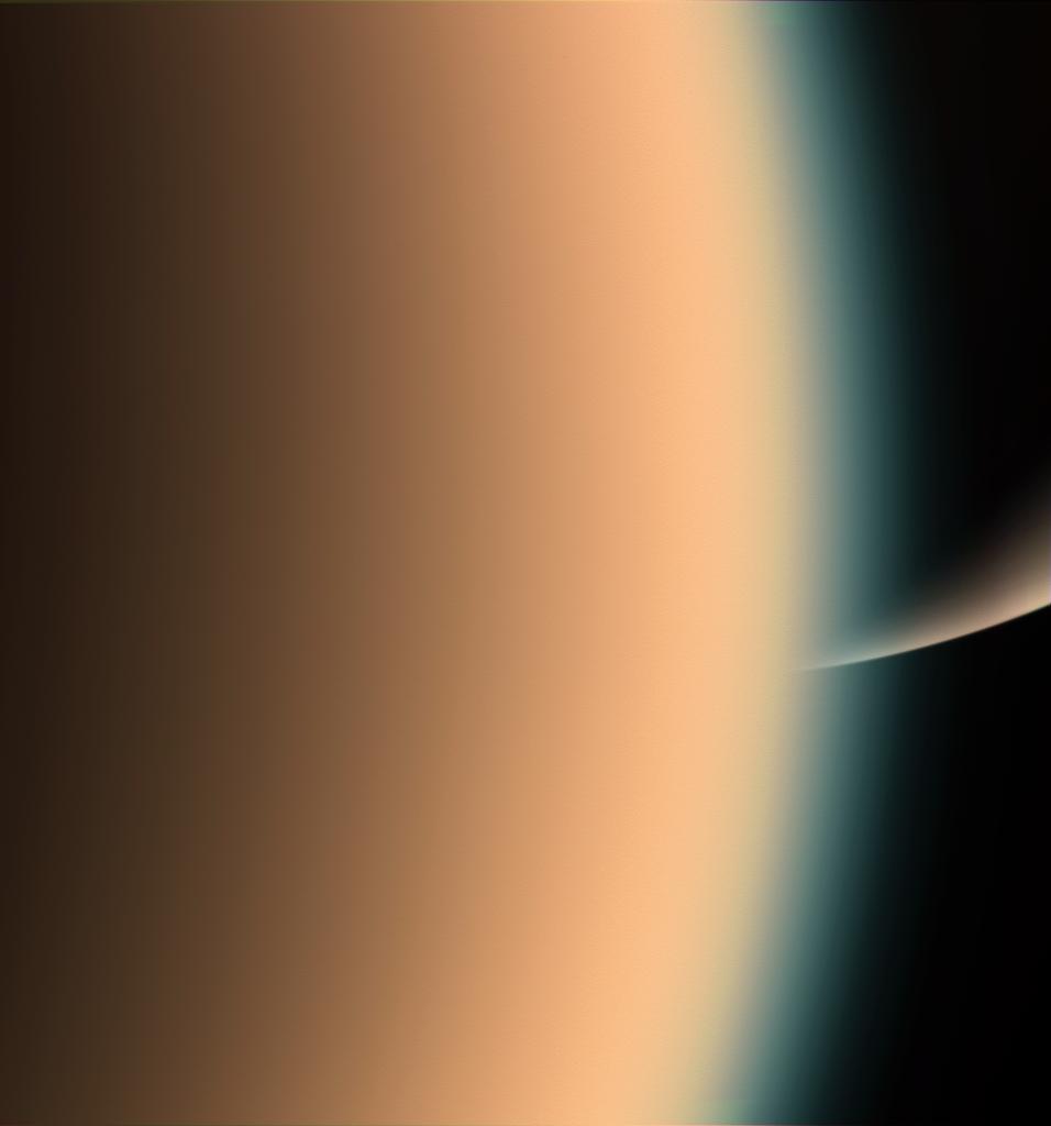 Cassini peers around the hazy limb of Titan to spy the sunlit south pole of Saturn in the distance beyond.