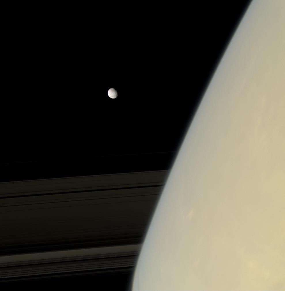 Mimas emerges from behind hazy Saturn.