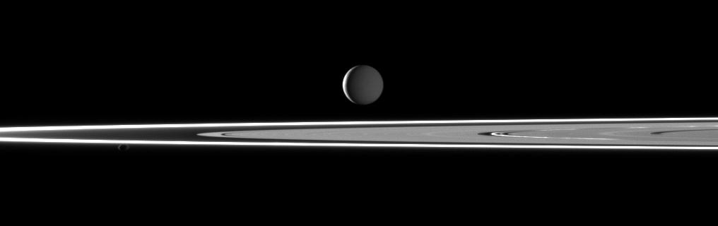 Two light sources illuminate Saturn's highly reflective moon Enceladus in this image featuring bright rings and the small moon Pandora in the foreground.