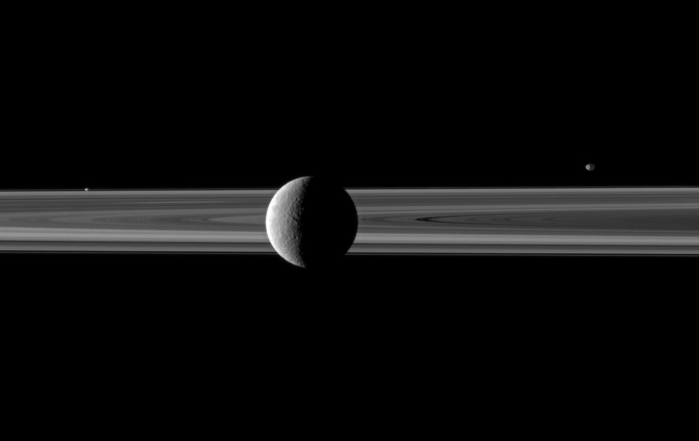Rhea in front of Saturn's rings, also visible are Janus and Prometheus