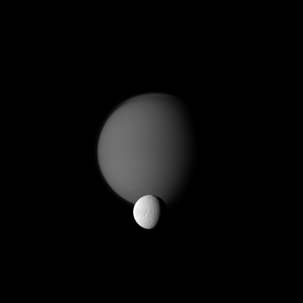 The Cassini spacecraft watches a pair of Saturn's moons, showing the hazy orb of giant Titan beyond smaller Tethys.