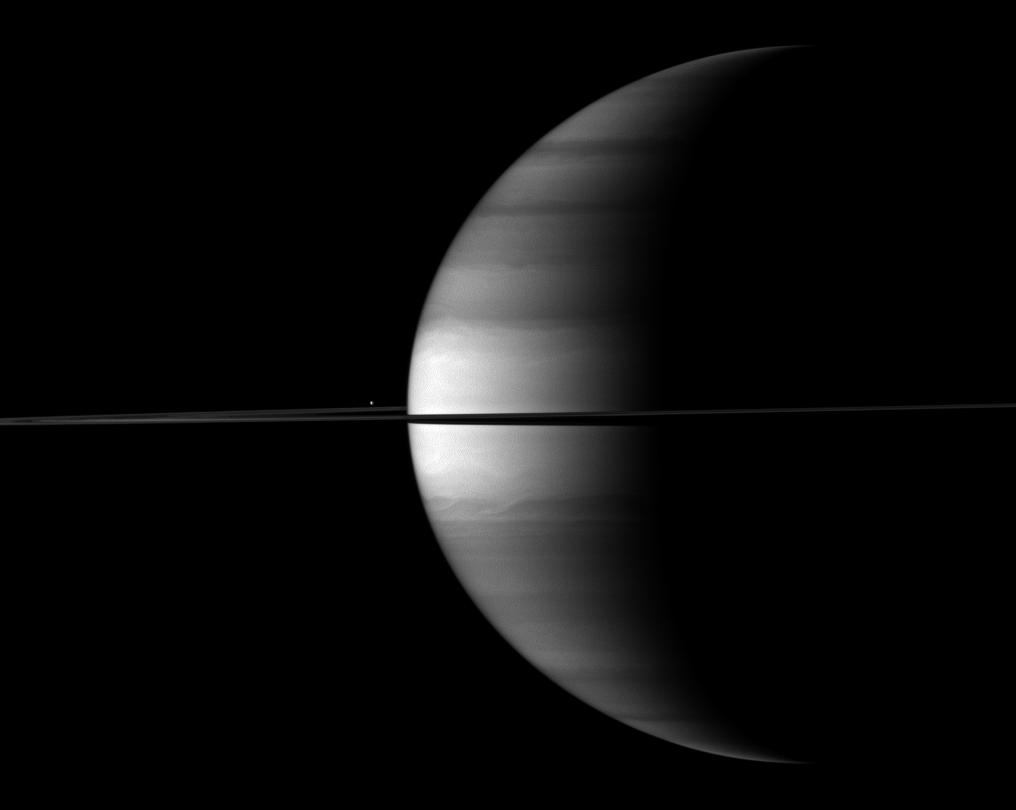 The highly reflective moon Enceladus appears as a bright dot beyond a crescent Saturn in this Cassini image.