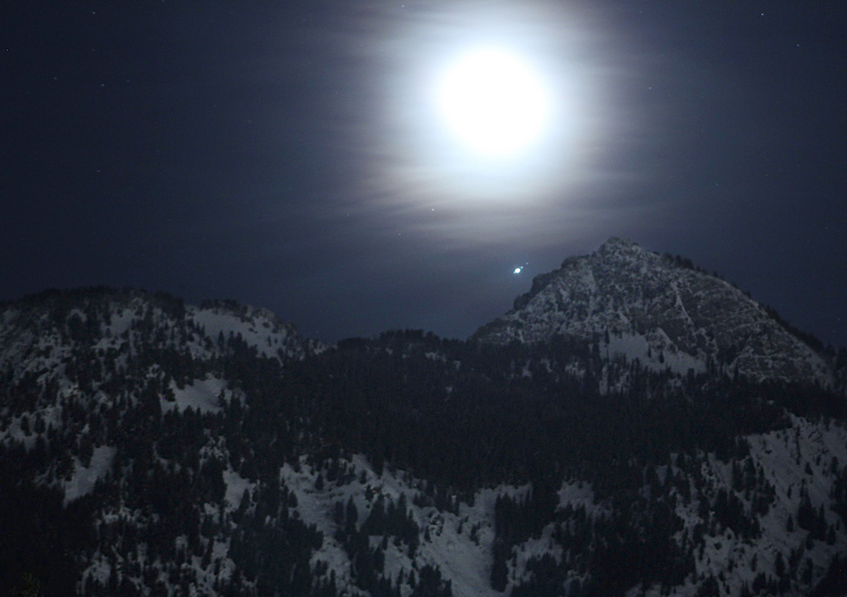 bright, hazy moon and stars above dark mountain range