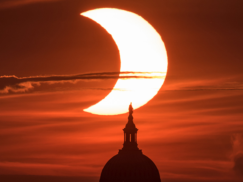 a photograph of a partial solar eclipse with the silhouette of the United States Capitol Building in the foreground