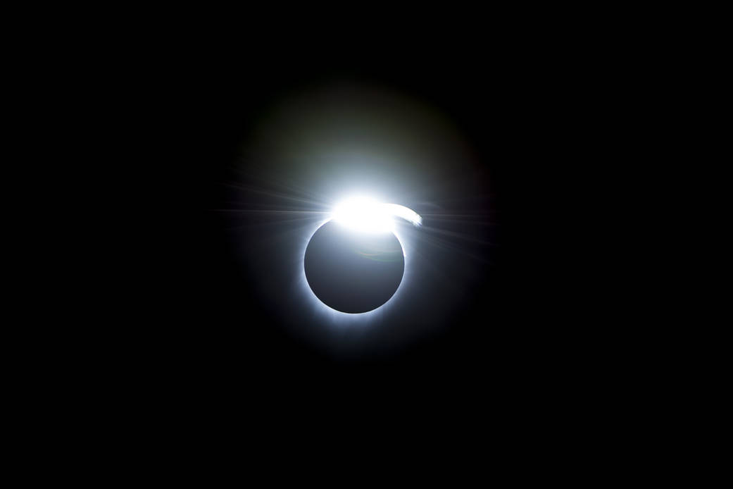A total solar eclipse against a dark sky, with a bright flash of light from the top of the eclipse where the Sun's light peaks around the Moon.